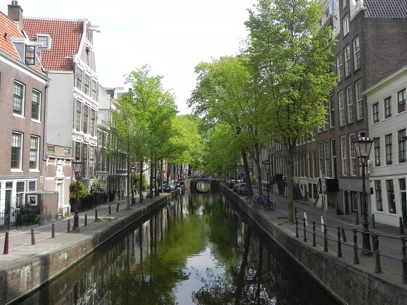 A canal in the old centre of Amsterdam lined with narrow brick canal houses and trees, seen along the water