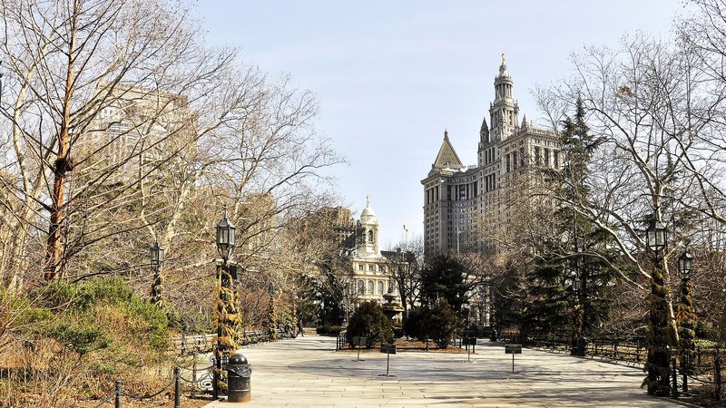 New York City Hall, a pale stone building with a clock-tower cupola, seen across City Hall Park with the Manhattan Municipal Building to the right