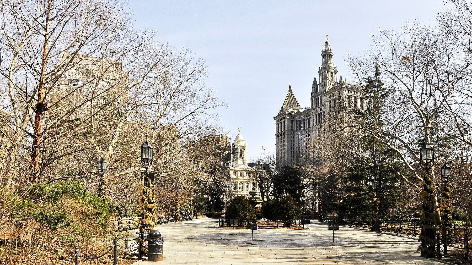 New York City Hall, a pale stone building with a clock-tower cupola, seen across City Hall Park with the Manhattan Municipal Building to the right