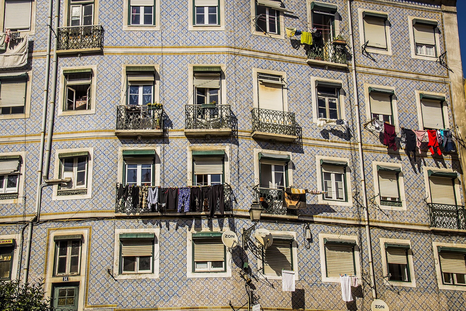 The blue and white tiled front of an apartment building in Lisbon's Alfama district, with iron balconies, shuttered windows and washing hung out to dry