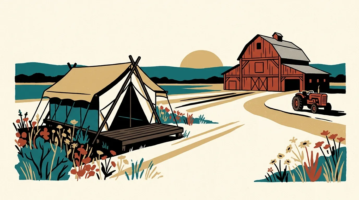 A canvas safari tent on a wooden platform sits in a field of wildflowers near a historic red barn under a golden late afternoon sky.