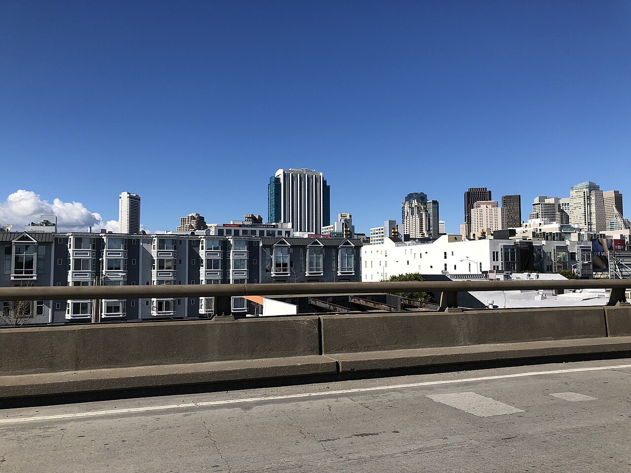 Rows of low apartment buildings below an elevated road, with a cluster of downtown towers on the skyline.