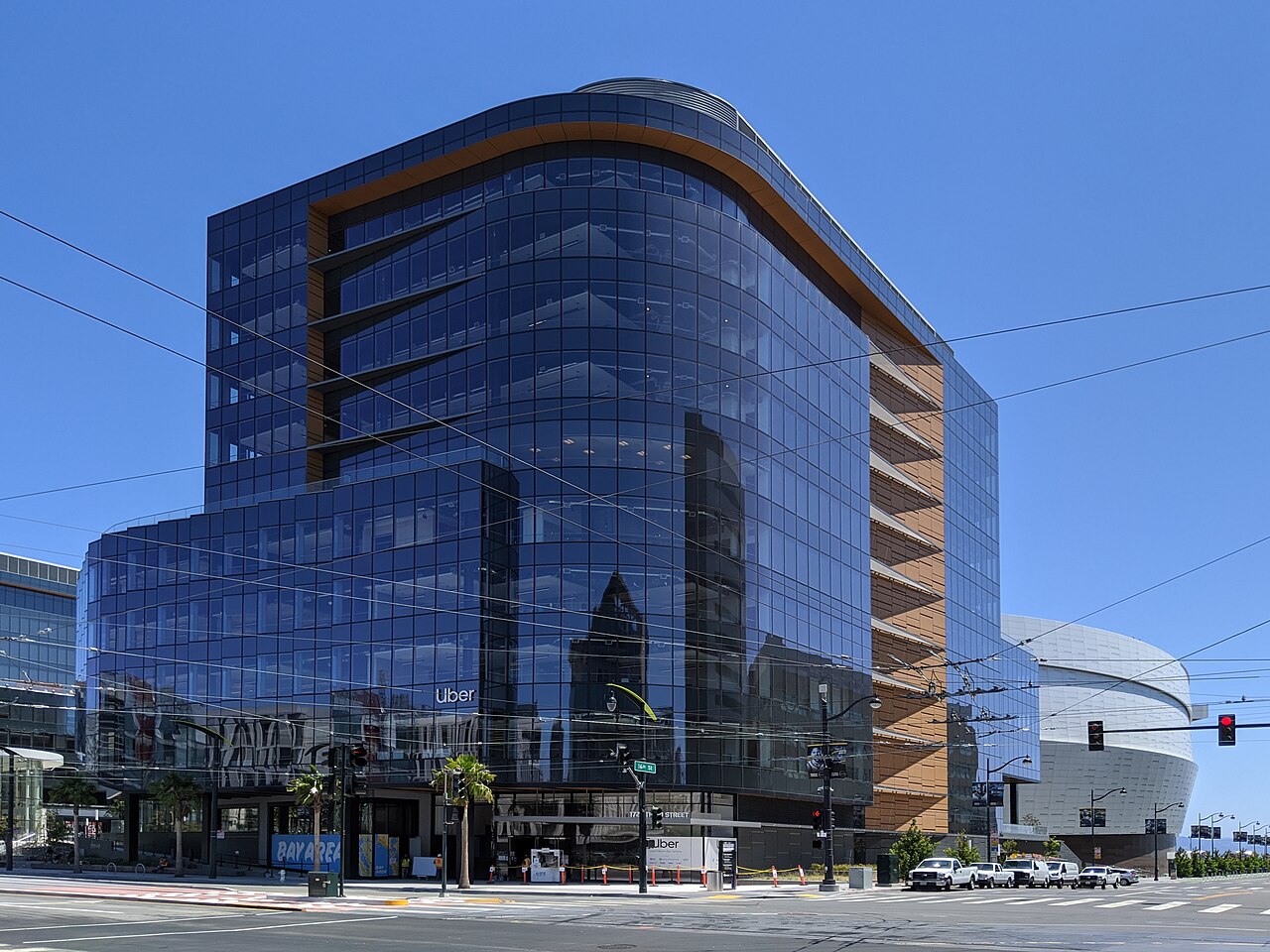 A blue glass office building with a curved copper-coloured edge on a street corner under a clear sky.