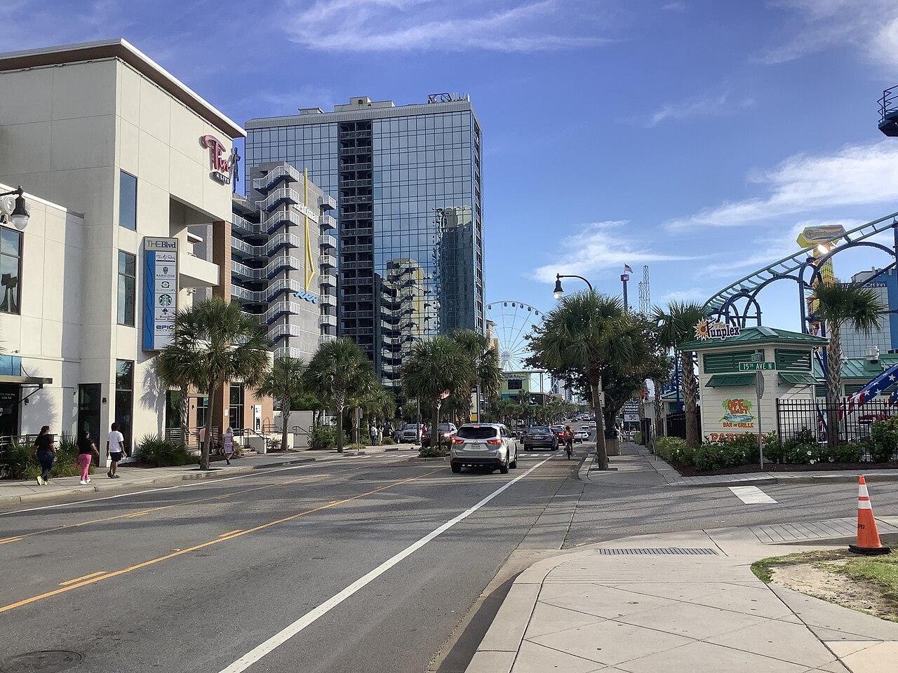 A street lined with palm trees and high-rise hotels, with a Ferris wheel in the distance.