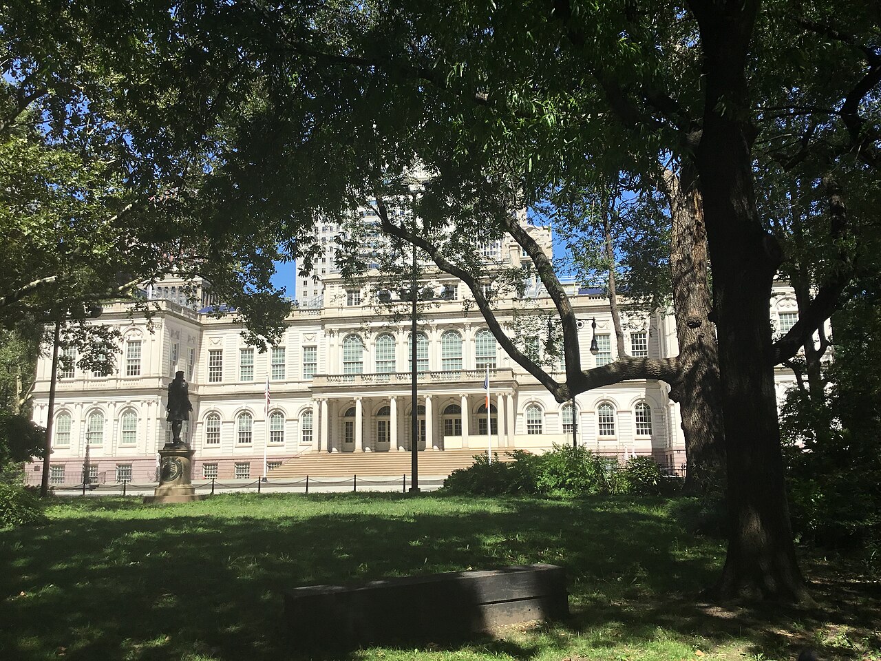 A white columned building with a central portico seen across a shaded lawn framed by large trees.