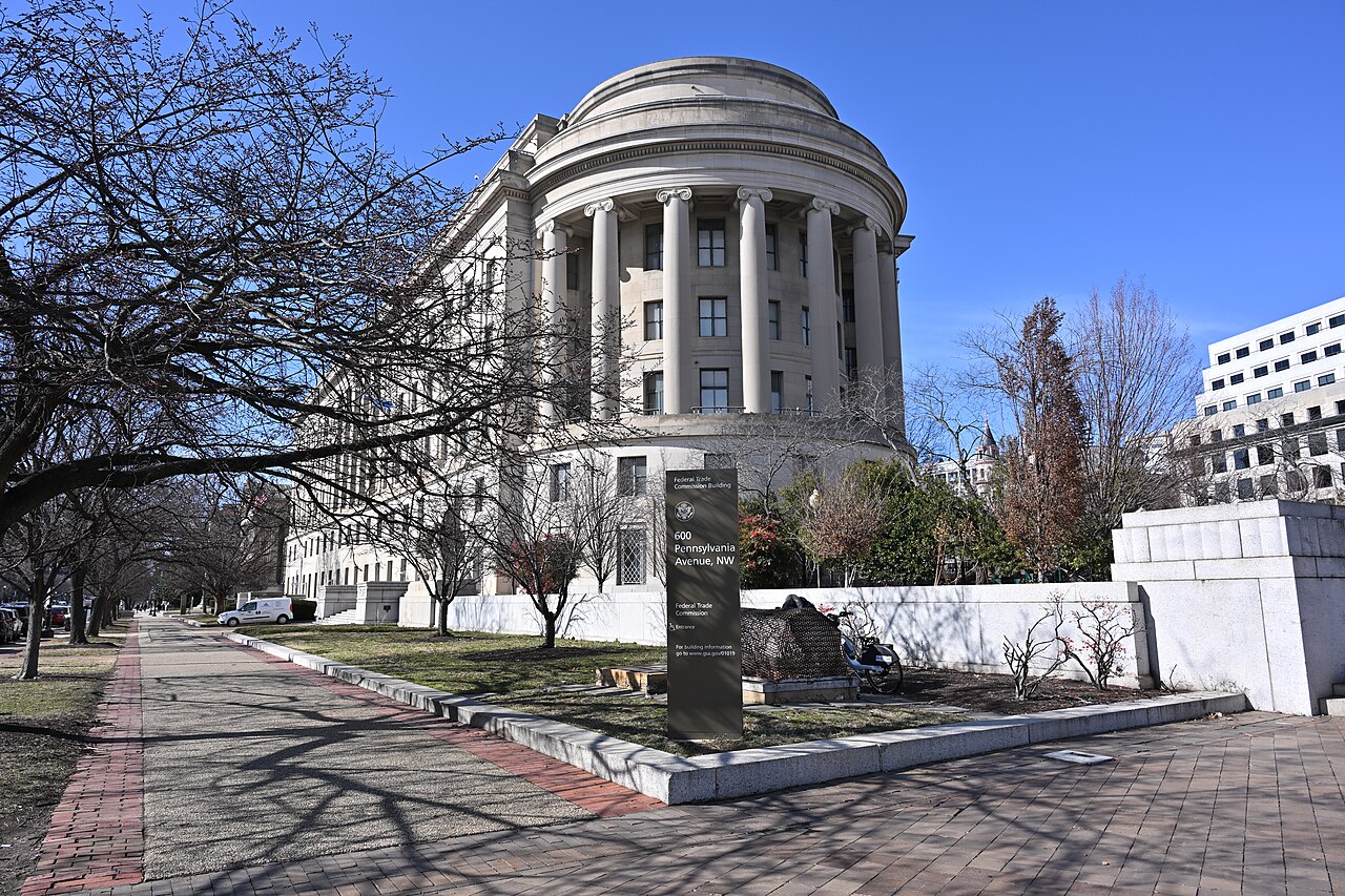 A pale stone building ends in a curved colonnade under a shallow dome, seen along a brick path past bare winter trees.