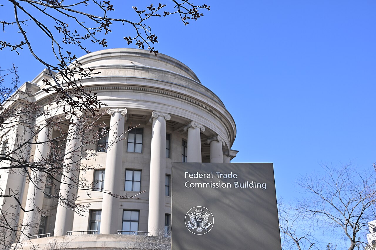 Tall white columns wrap around the rounded end of a stone building under a clear blue sky, with bare branches in front.