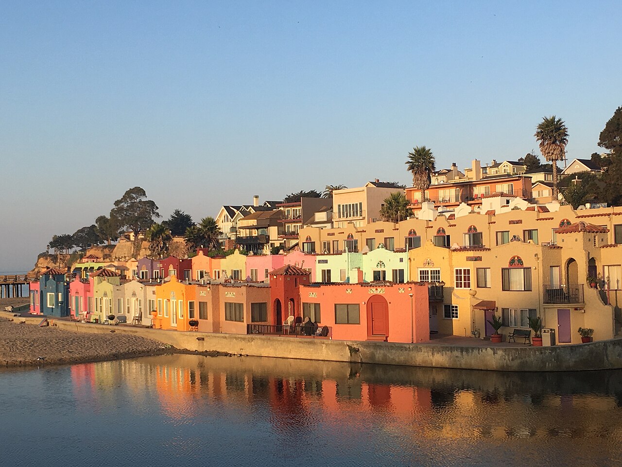 Rows of small pink, orange and yellow stucco houses step down to still water that mirrors them in warm light.