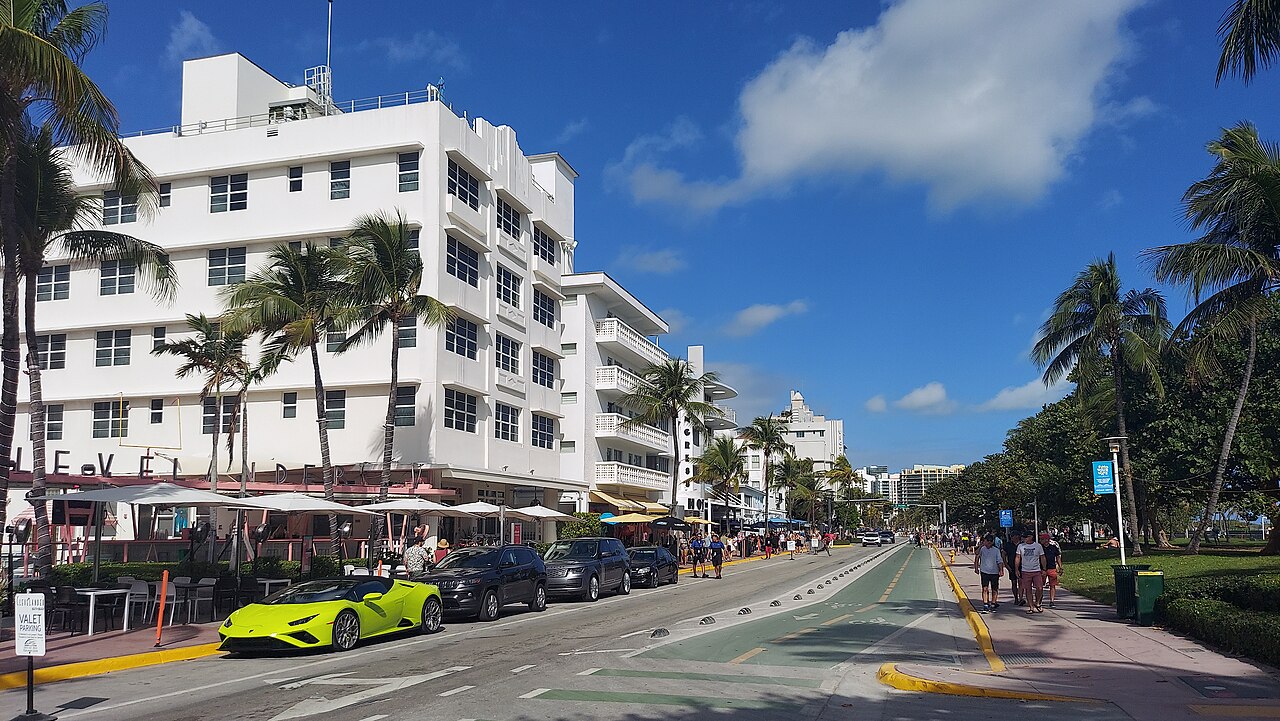 A street of white multi-storey hotels with terraces and palm trees runs into the distance, cars parked along the kerb.