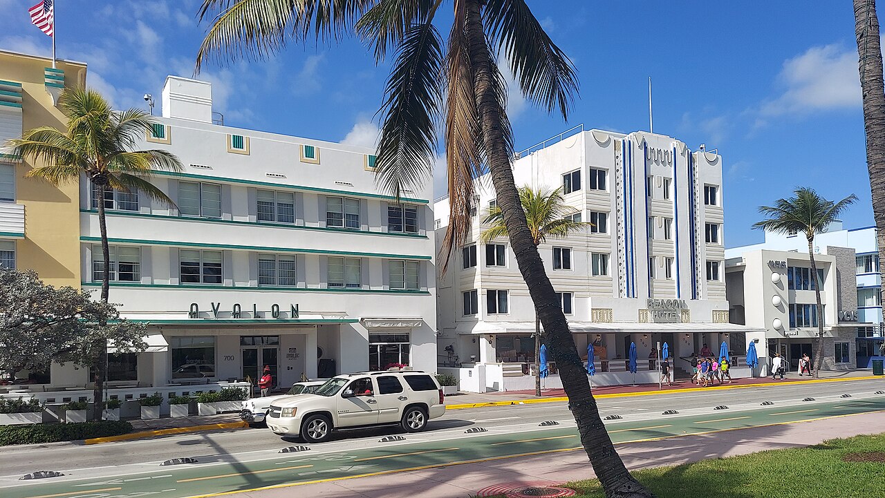Low white hotels with pastel trim line a street behind a leaning palm tree under a deep blue sky.