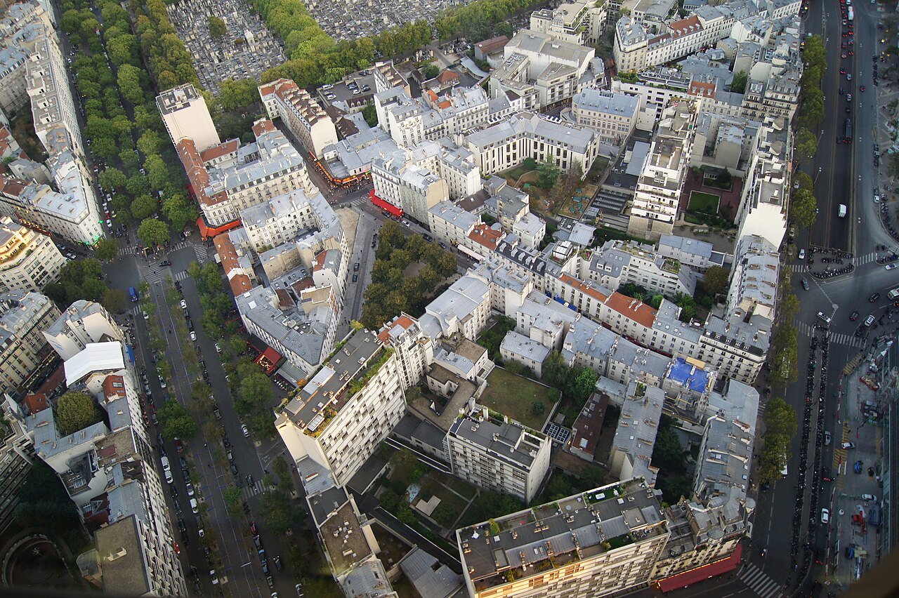Dense blocks of grey-roofed apartment buildings and tree-lined streets seen from high above.