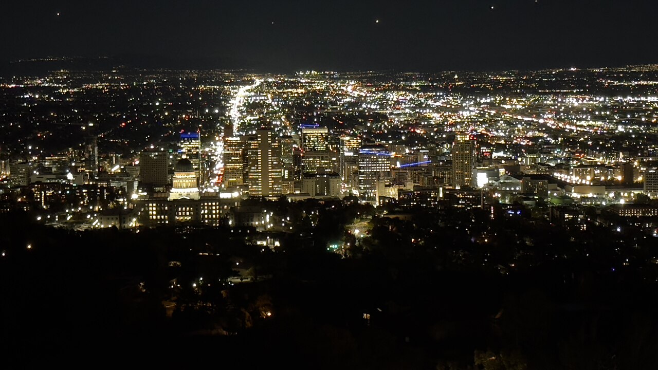 A grid of city lights spreads across a dark valley, with a cluster of lit towers at the left.