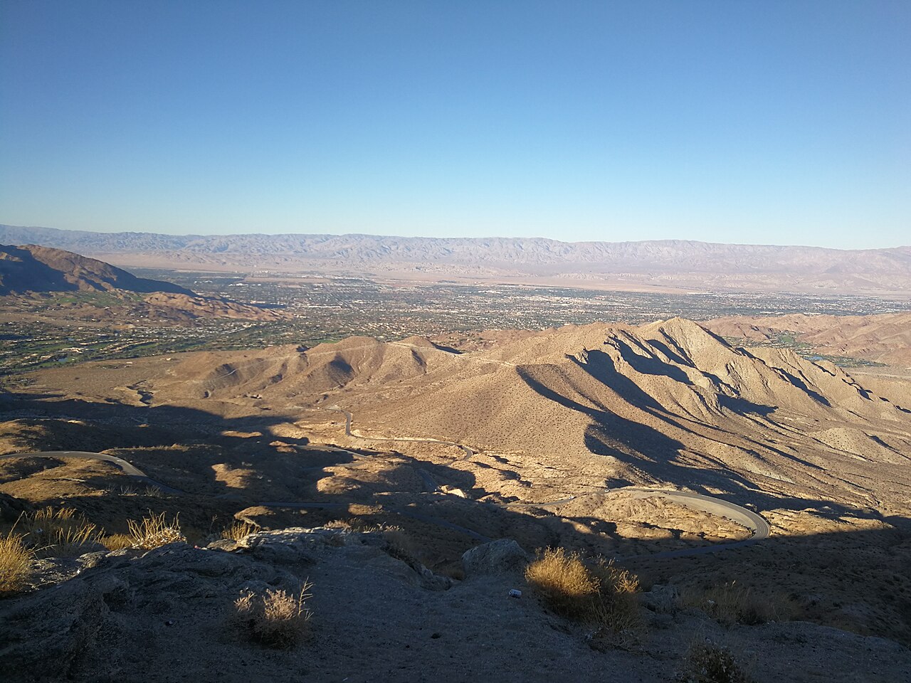 Bare desert ridges fall away to a wide flat valley with a city spread across its floor.