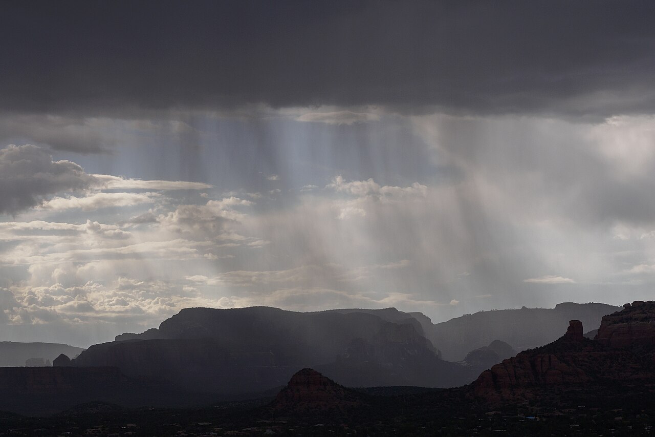 Shafts of rain hang from dark clouds above a line of flat-topped ridges.