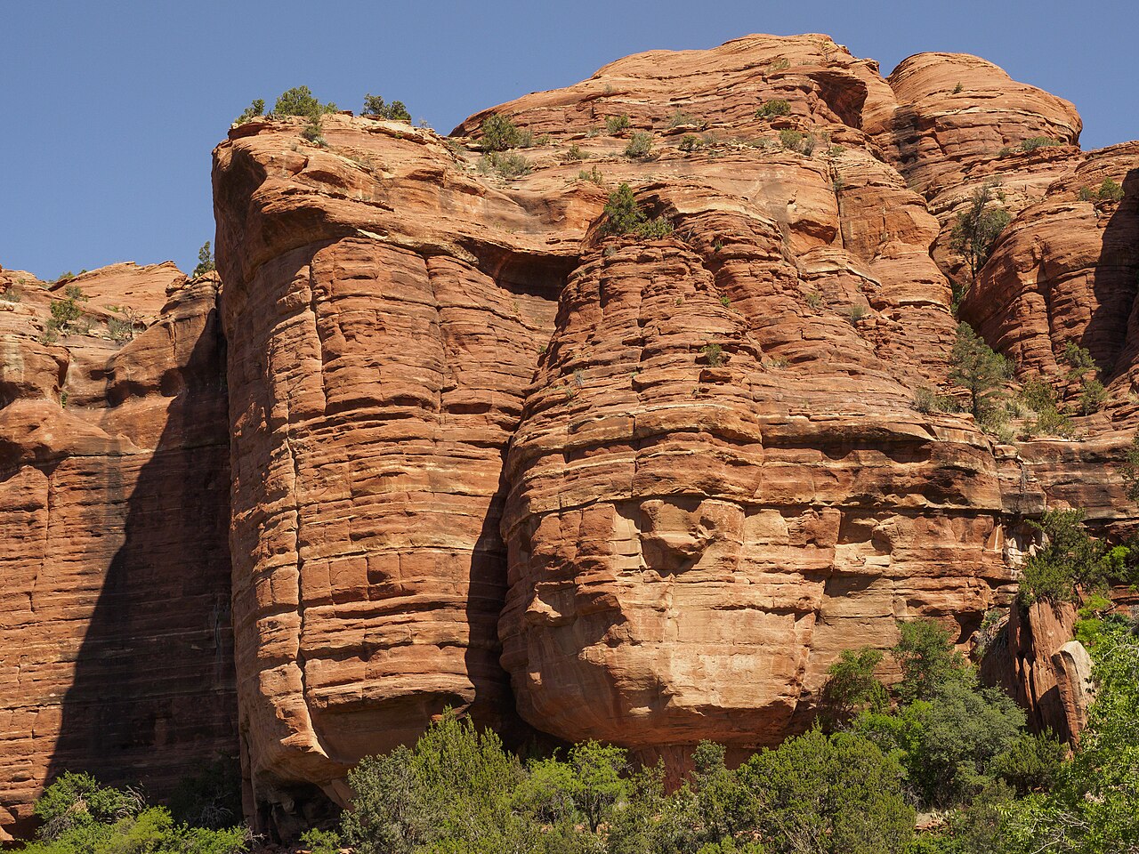 Rounded red sandstone cliffs rise above green scrub under a blue sky.