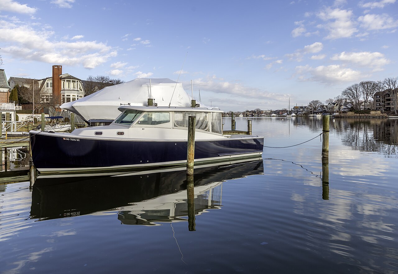 A dark-hulled motor yacht sits at a piling on still water that mirrors the boat and the sky.
