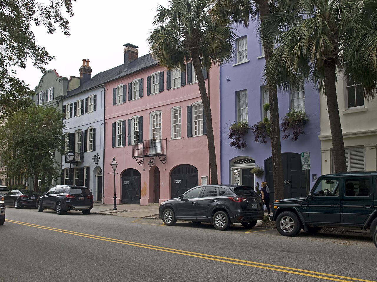 A terrace of pastel pink, lilac and cream townhouses stands behind palm trees and parked cars.