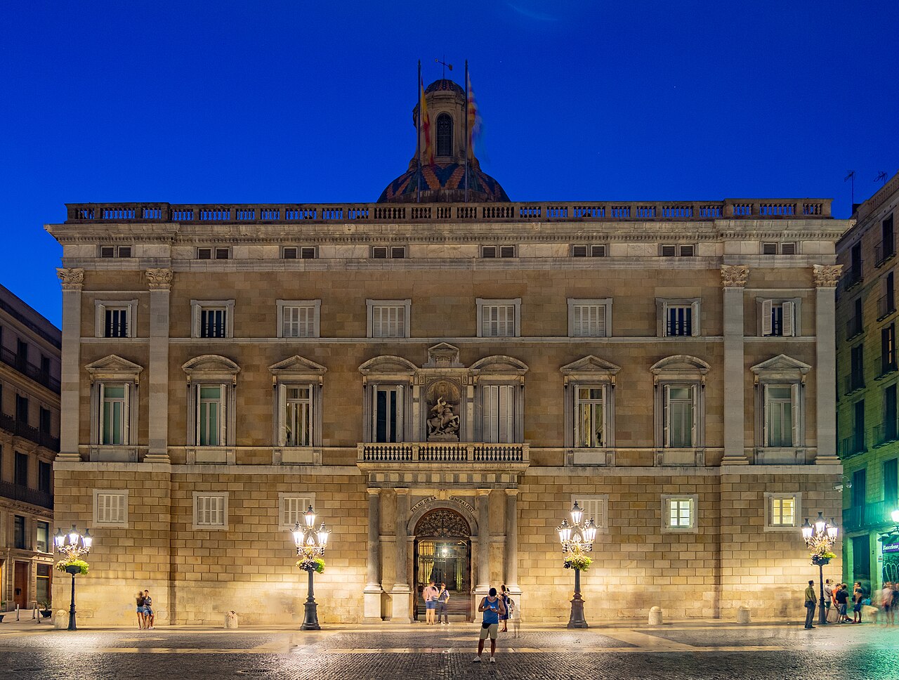 A floodlit stone palace with a small dome faces an open square under a deep blue sky.