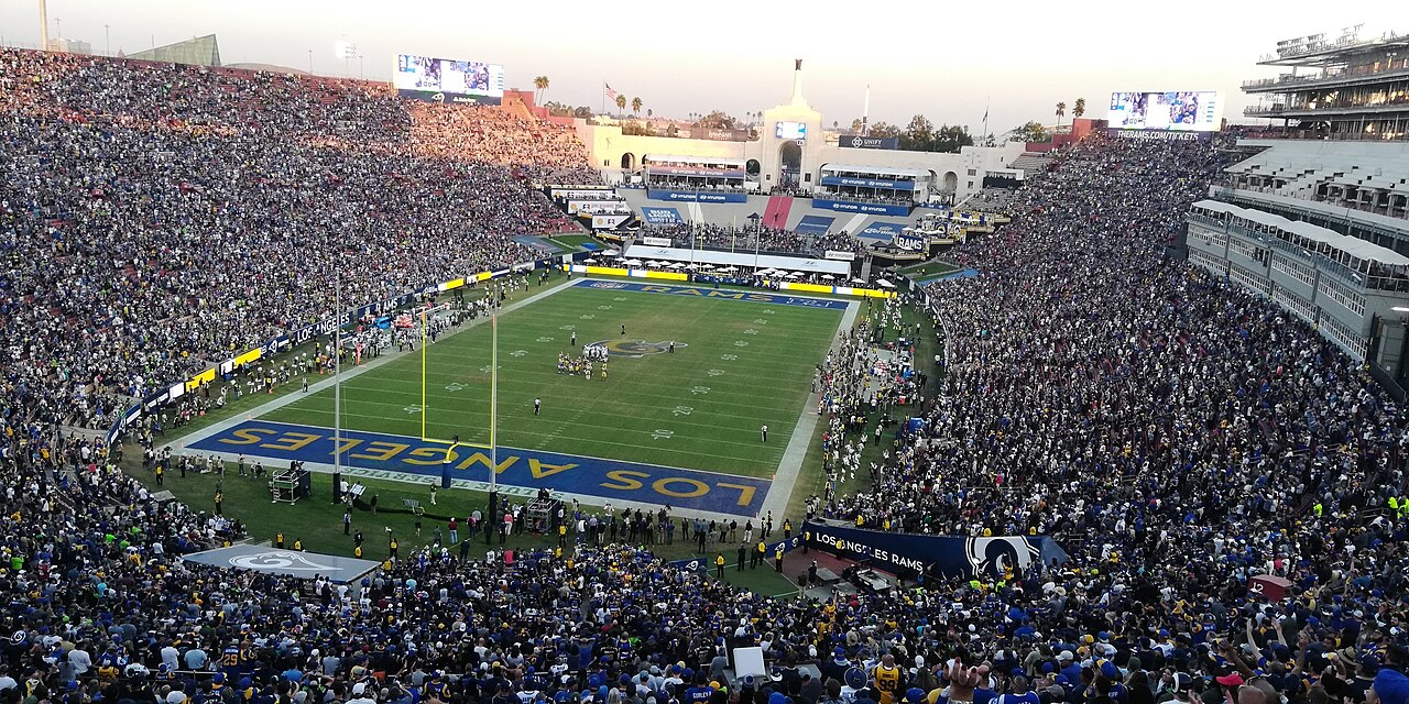 A full oval stadium seen from high in the stands, with a green football field in the middle and the arched peristyle at the far end.
