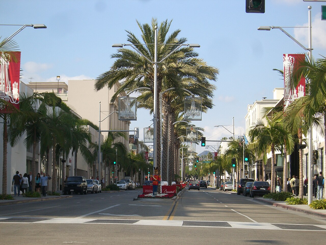 A wide street running into the distance between low shop buildings, with tall palm trees down the middle and along both sides.