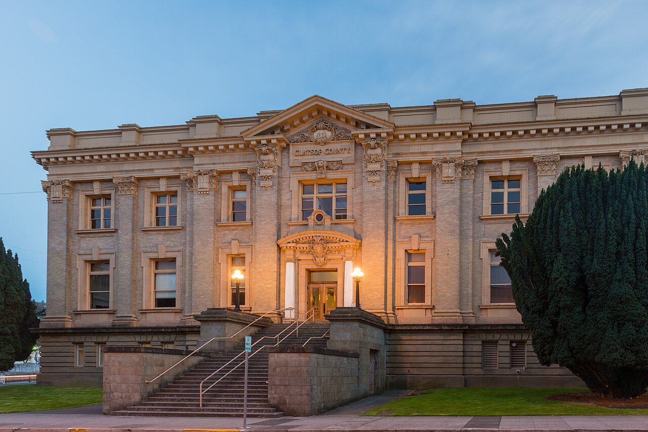 A pale stone courthouse with classical columns and a lit entrance at the top of a flight of steps under a deep blue sky.
