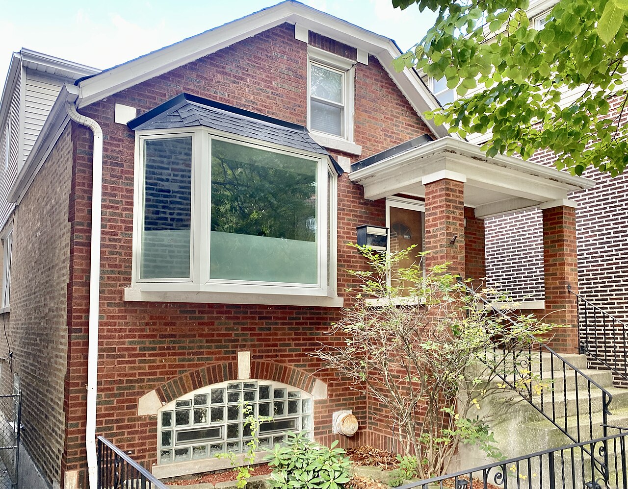 A red brick house with a large bay window and a short flight of steps up to a covered front door.