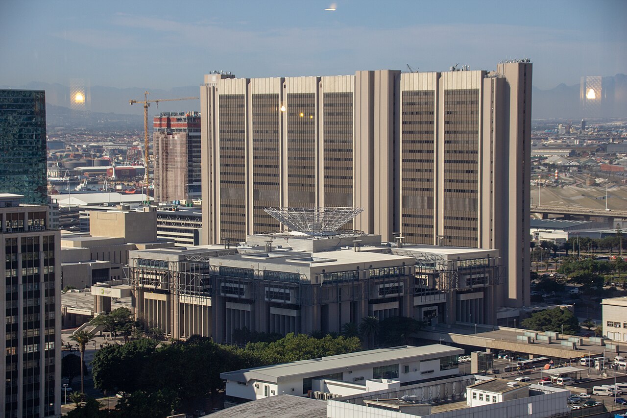 A wide beige tower block rises above lower office buildings and rooftops, with flat land stretching to the horizon behind it.