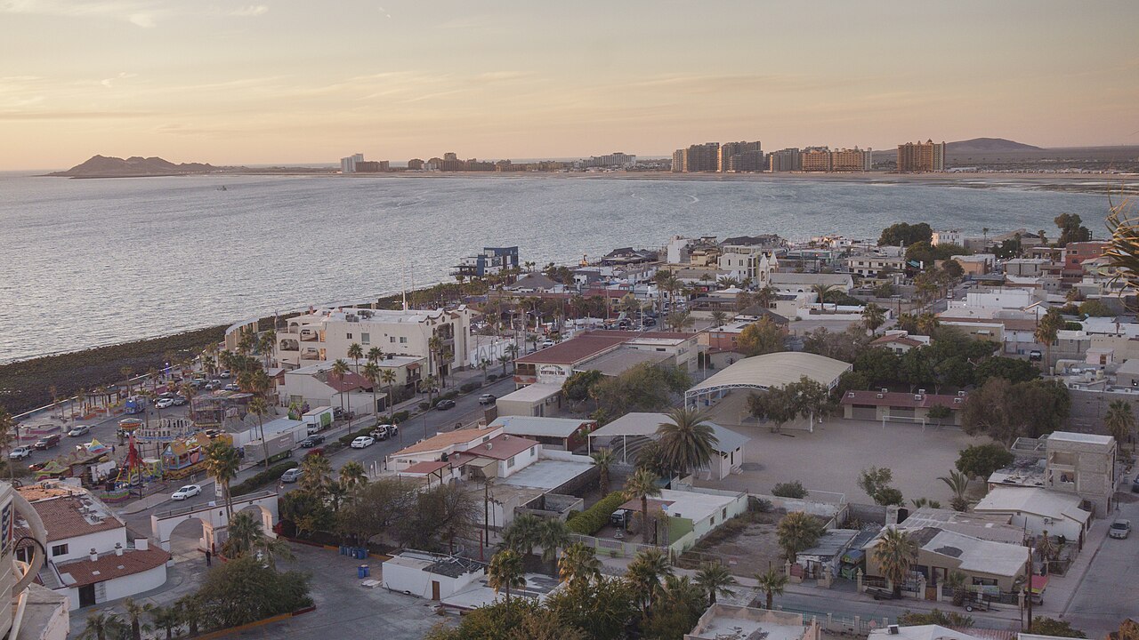 Low houses and streets of a seaside town run down to a bay, with a row of high-rise blocks on the far shore.