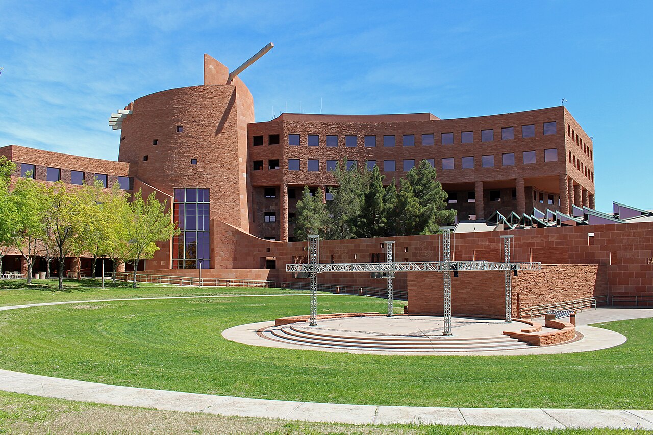 Curved red sandstone buildings with a round tower wrap around a lawn and a small circular outdoor stage.