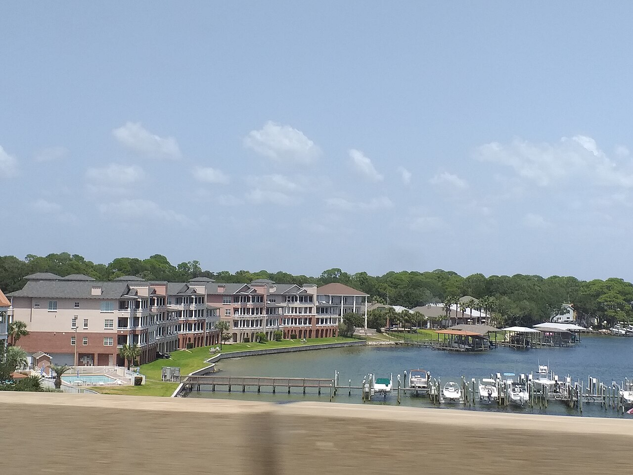 Pastel low-rise buildings and a row of boat docks line a calm blue inlet backed by trees.