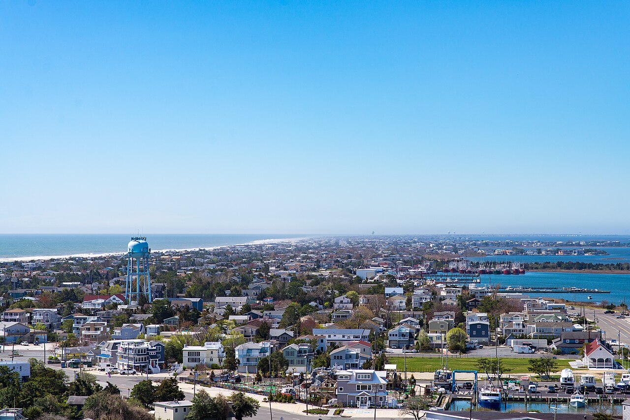 A narrow, low-lying strip of land covered with houses and trees runs into the distance between ocean and bay.