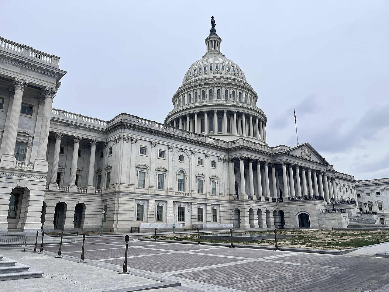 A long white stone building with columned wings and a large central dome, seen at an angle across an empty plaza.