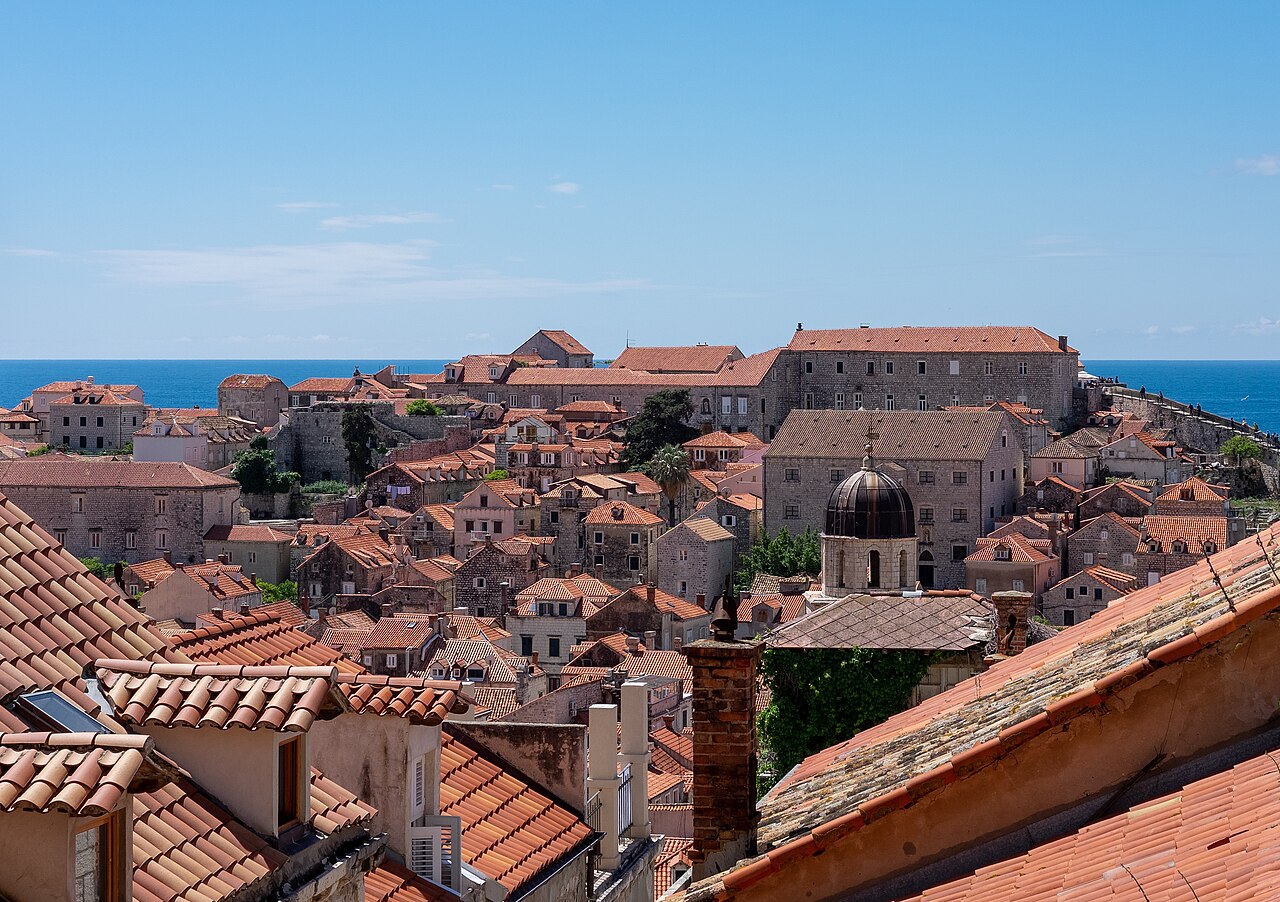 A dense vista of orange tiled rooftops and stone buildings leading out towards the blue open sea.