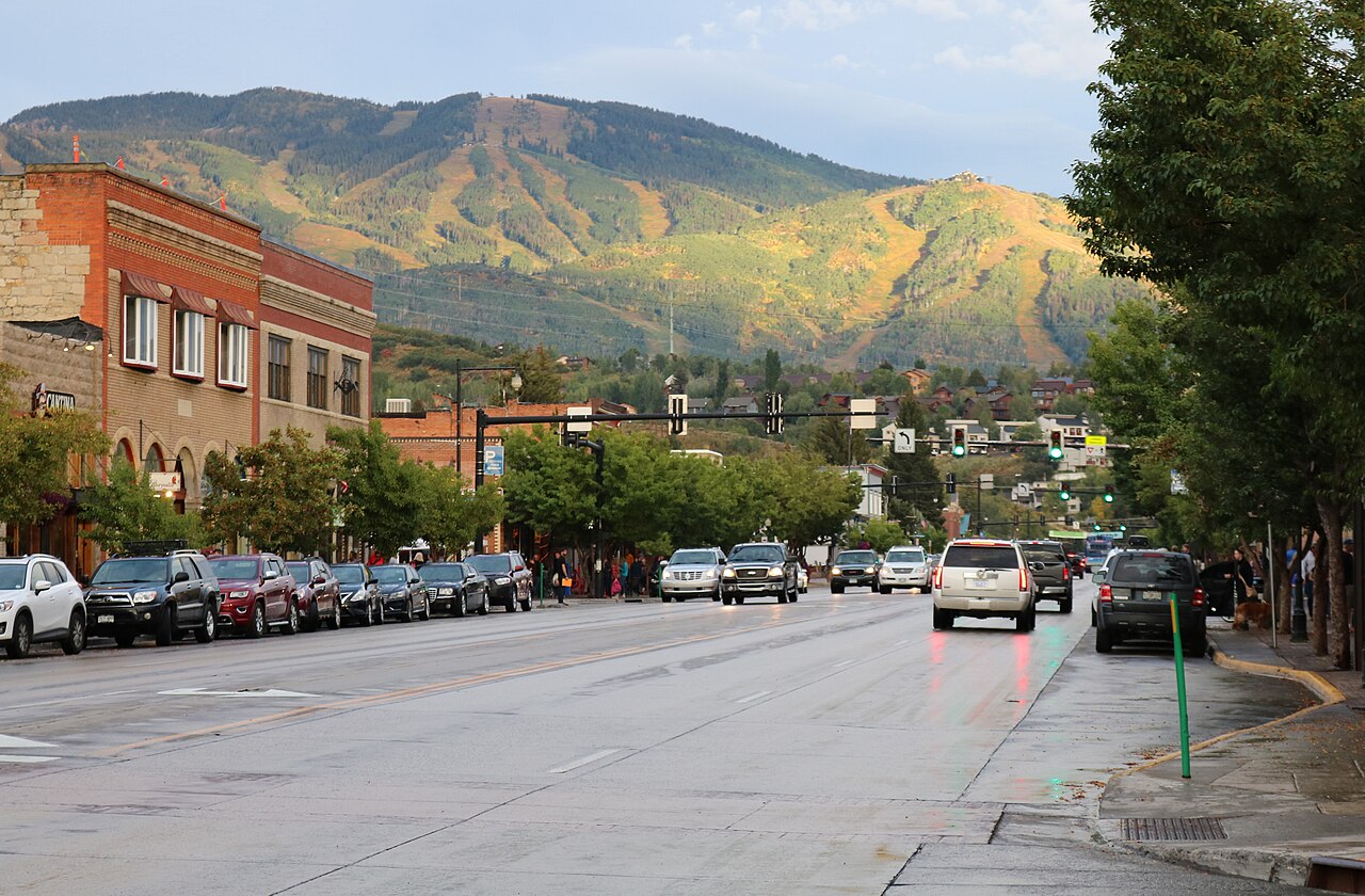 A broad forested mountain marked with ski runs rises behind a small town street.