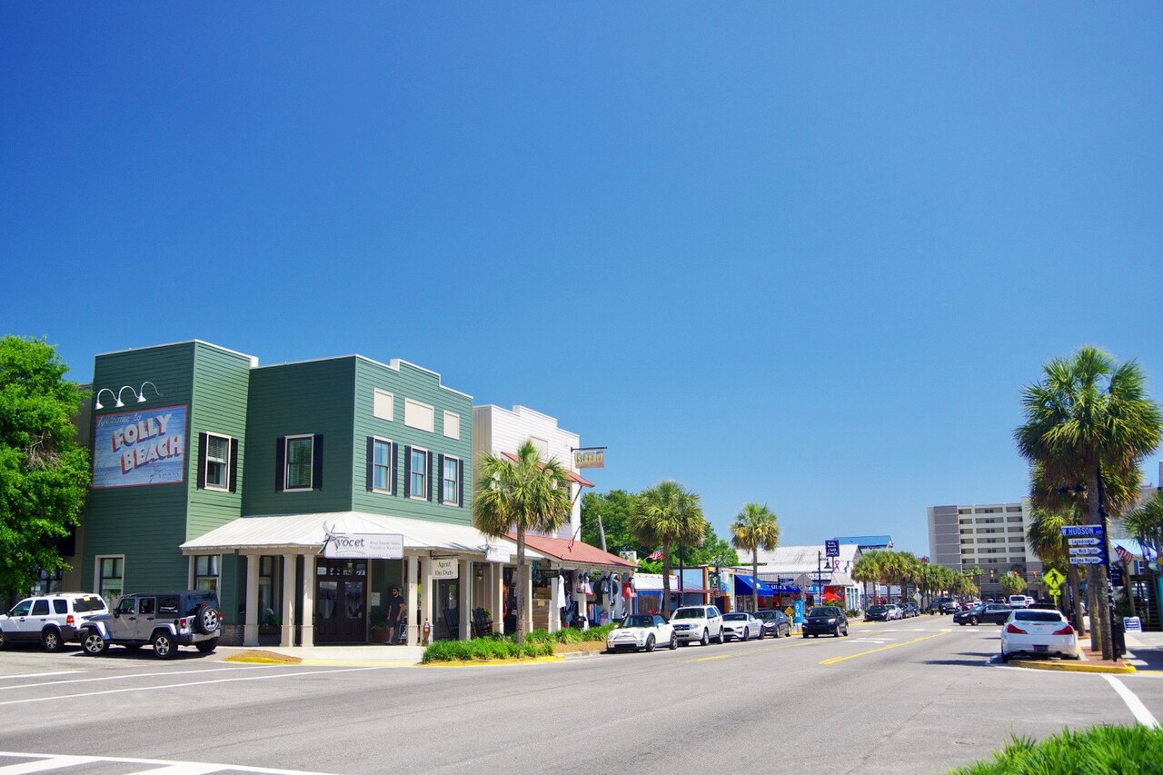 A sunny main street with a green two-storey corner building, palm trees, low shops and parked cars.