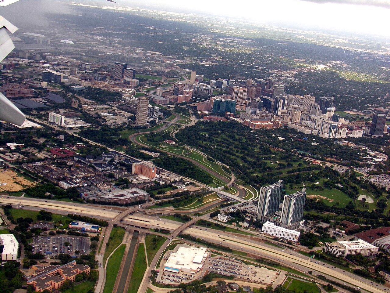 An aerial view of a dense cluster of high-rise buildings surrounded by parkland, highways and low suburbs.
