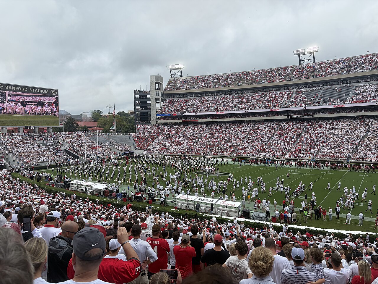A packed football stadium seen from the stands, the crowd almost all in white, with a band formed up on the field.