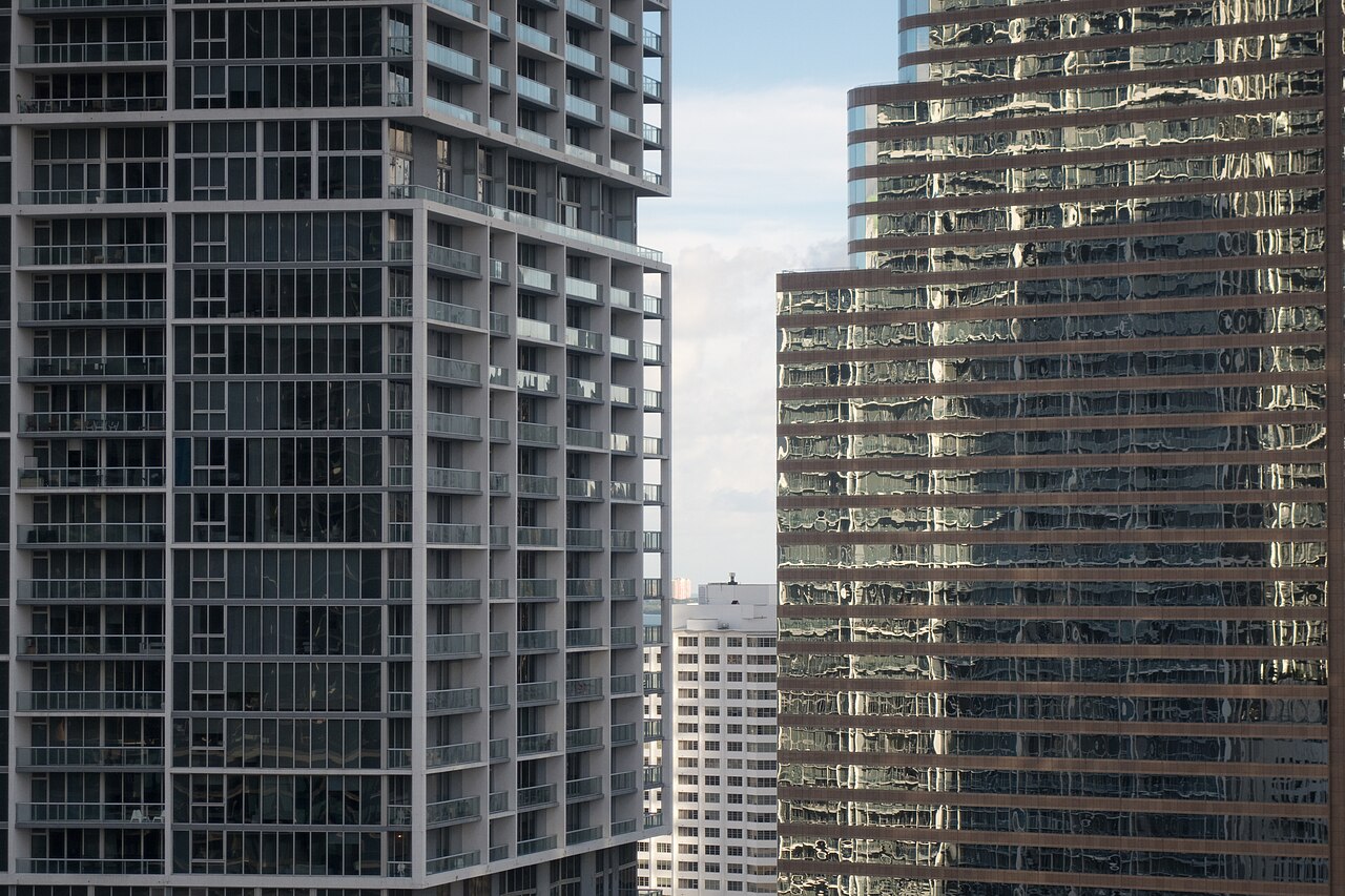 Two tall apartment towers lined with rows of balconies, seen close up, with more towers between them in the distance.