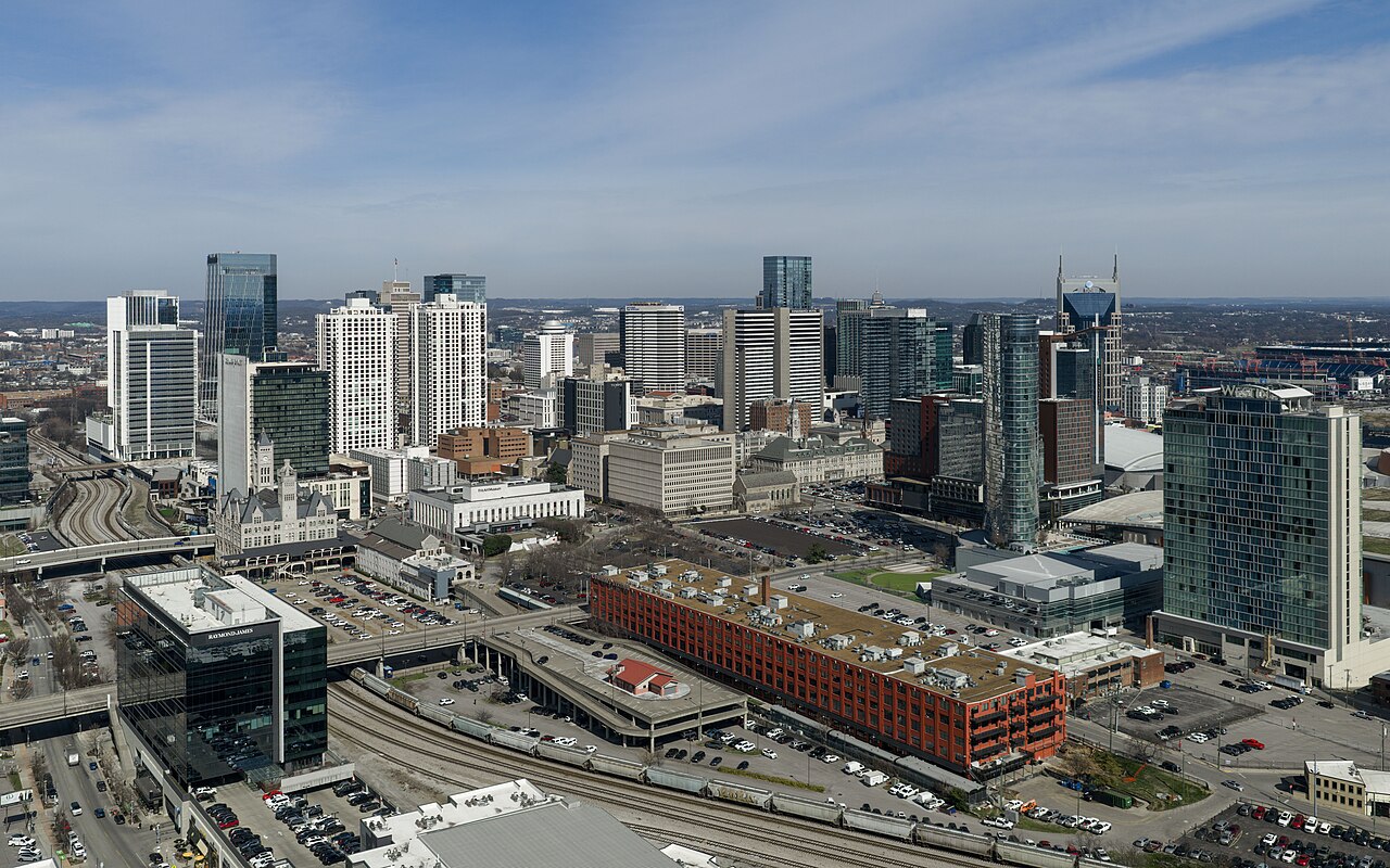 An aerial view of a downtown of glass towers, with rail yards and a long red brick building in the foreground.
