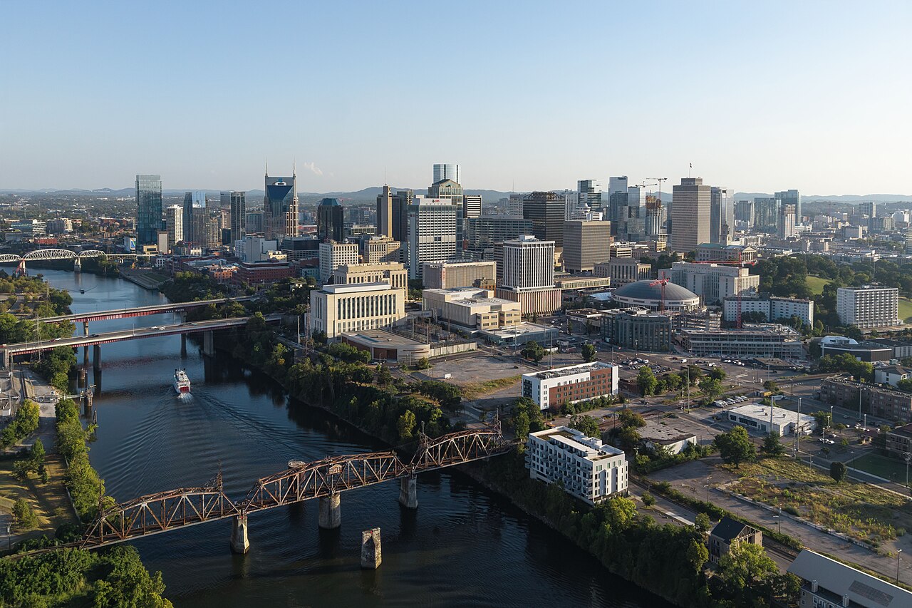 An aerial view of a river crossed by several bridges, curving past a downtown skyline in low sunlight.