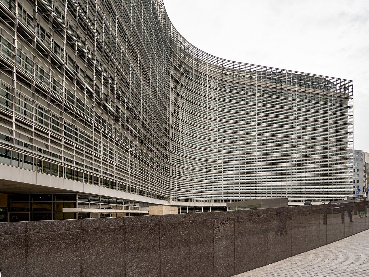 The long curved front of a many-storeyed office building covered in horizontal metal louvres.