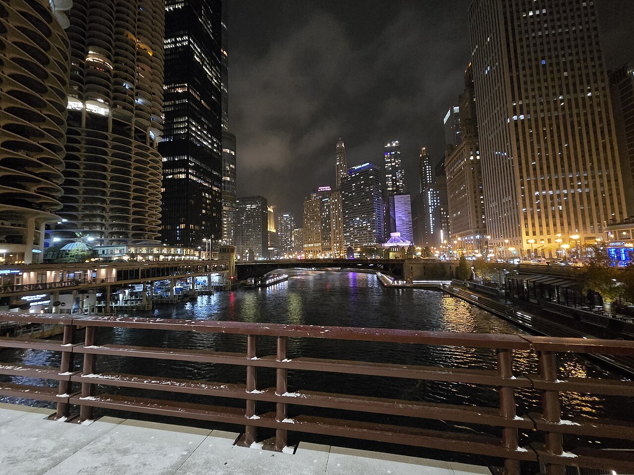Lit towers on both banks of a river at night, viewed over the railing of a bridge.