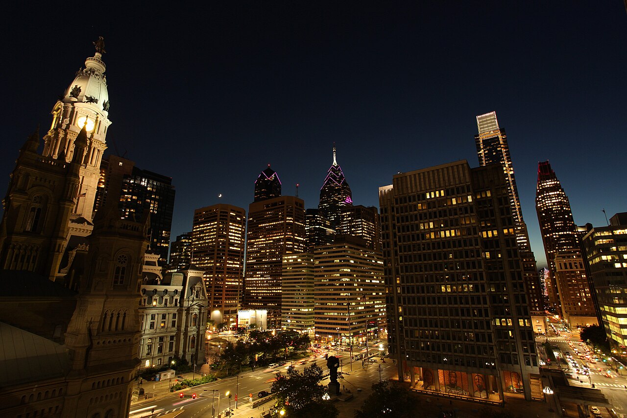 A night view over lit office and apartment towers with an ornate stone tower in the left foreground.