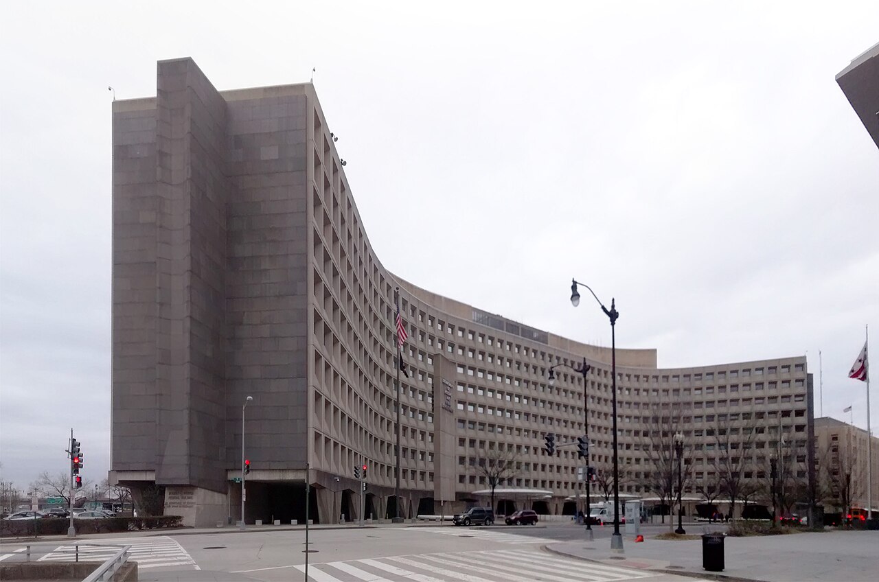A long curved concrete office building with rows of deep-set square windows, seen from across a street.