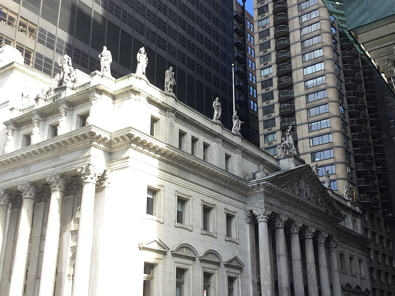 A white marble courthouse with columns and rooftop statues, set against dark glass towers.