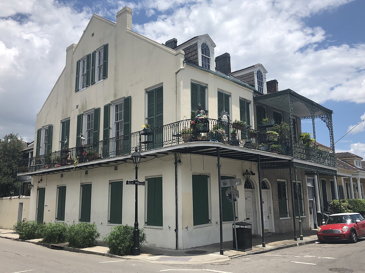 A cream three-storey corner house with green shutters and an iron balcony wrapping around the first floor.