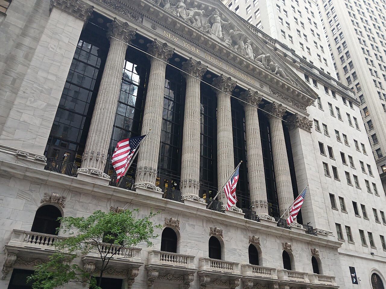 Tall stone columns under a carved pediment on a classical building, with three American flags hanging at street level.