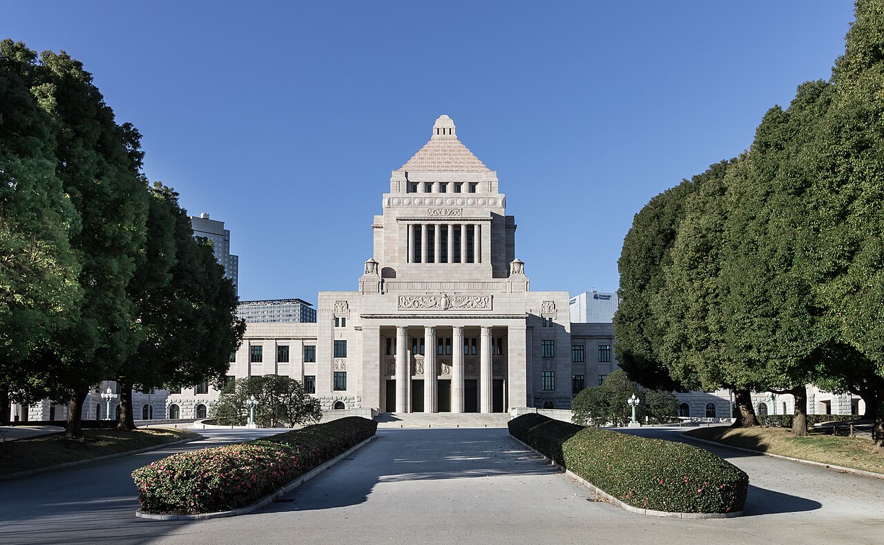 A pale stone building with a stepped pyramid tower and a columned entrance at the end of a tree-lined drive.