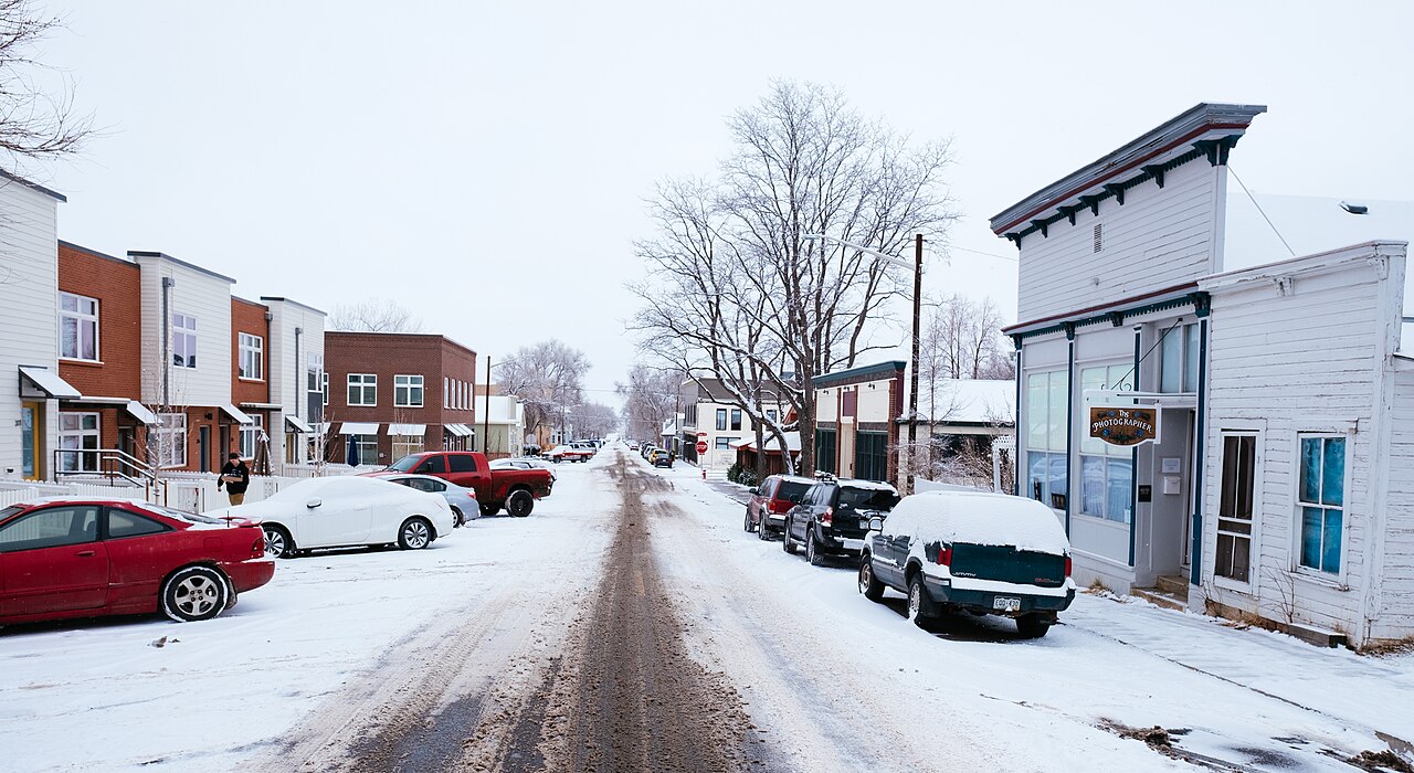 A snow-dusted street lined with cars and small buildings leads toward the horizon.