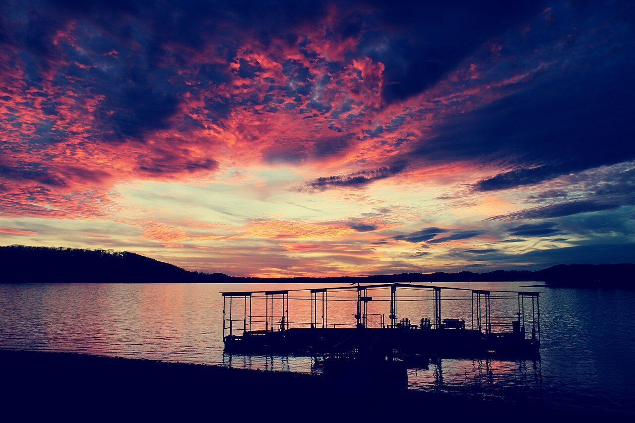 A floating dock in silhouette on calm water under a sky of red and orange clouds.